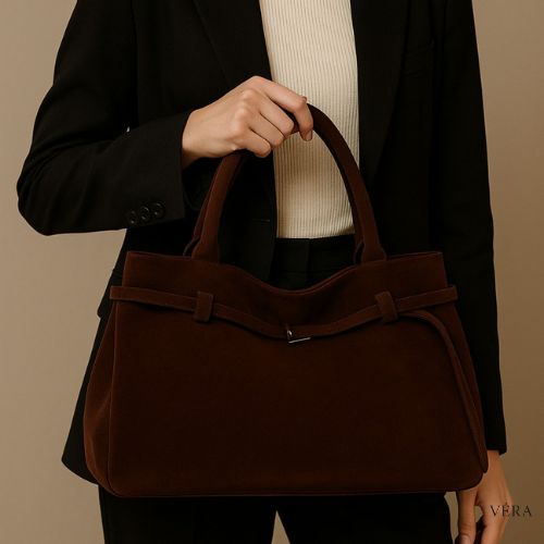 Bolso de gamuza marrón sobre sofá blanco con decoración minimalista
